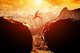 A person jumping over a chasm between two protruding rocks with jagged mountains in the background [Image by creator Photocreo Bednarek from AdobeStock]